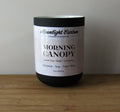 Coconut, soy, and palm wax candle labeled 'Morning Canopy' by Moonlight Carbon on a wooden surface with a neutral background. Fragrance notes include green tea, rose, and cardamon. 