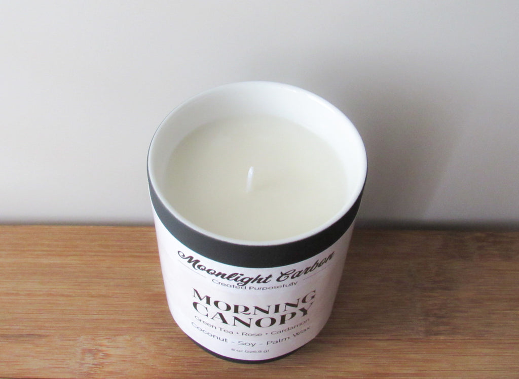 Zoomed in look at the coconut soy wax candle in a black ceramic container with beige label on a wooden surface. In the center of the candle is a cotton wick.