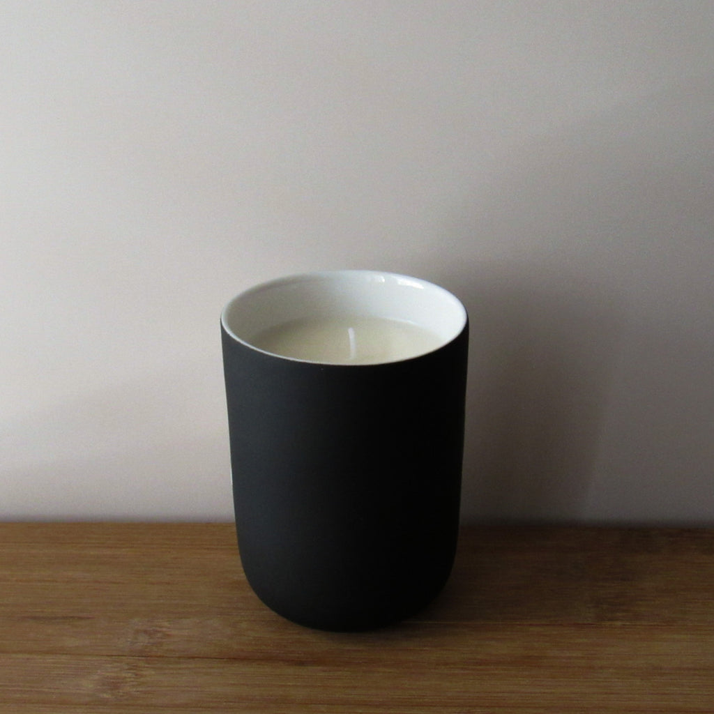Black ceramic candle with white interior on a wooden surface and light gray background