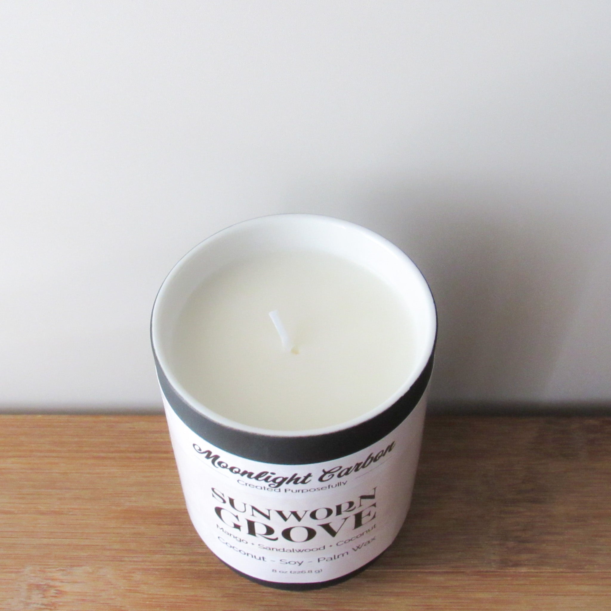 Zoomed in look at the coconut soy wax candle in a black ceramic container with beige label on a wooden surface. In the center of the candle is a cotton wick.