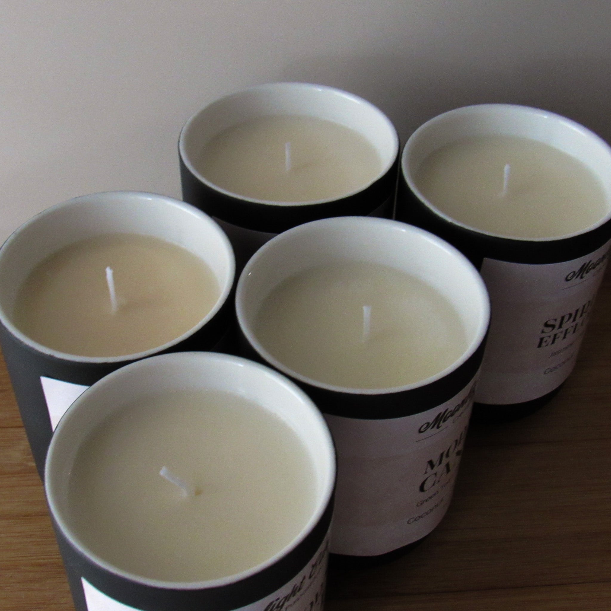 Five candles in black ceramic containers on a wooden surface with a neutral background