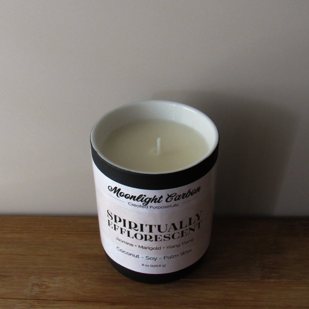 Zoomed in look at the coconut soy wax candle in a black ceramic container with beige label on a wooden surface. In the center of the candle is a cotton wick.