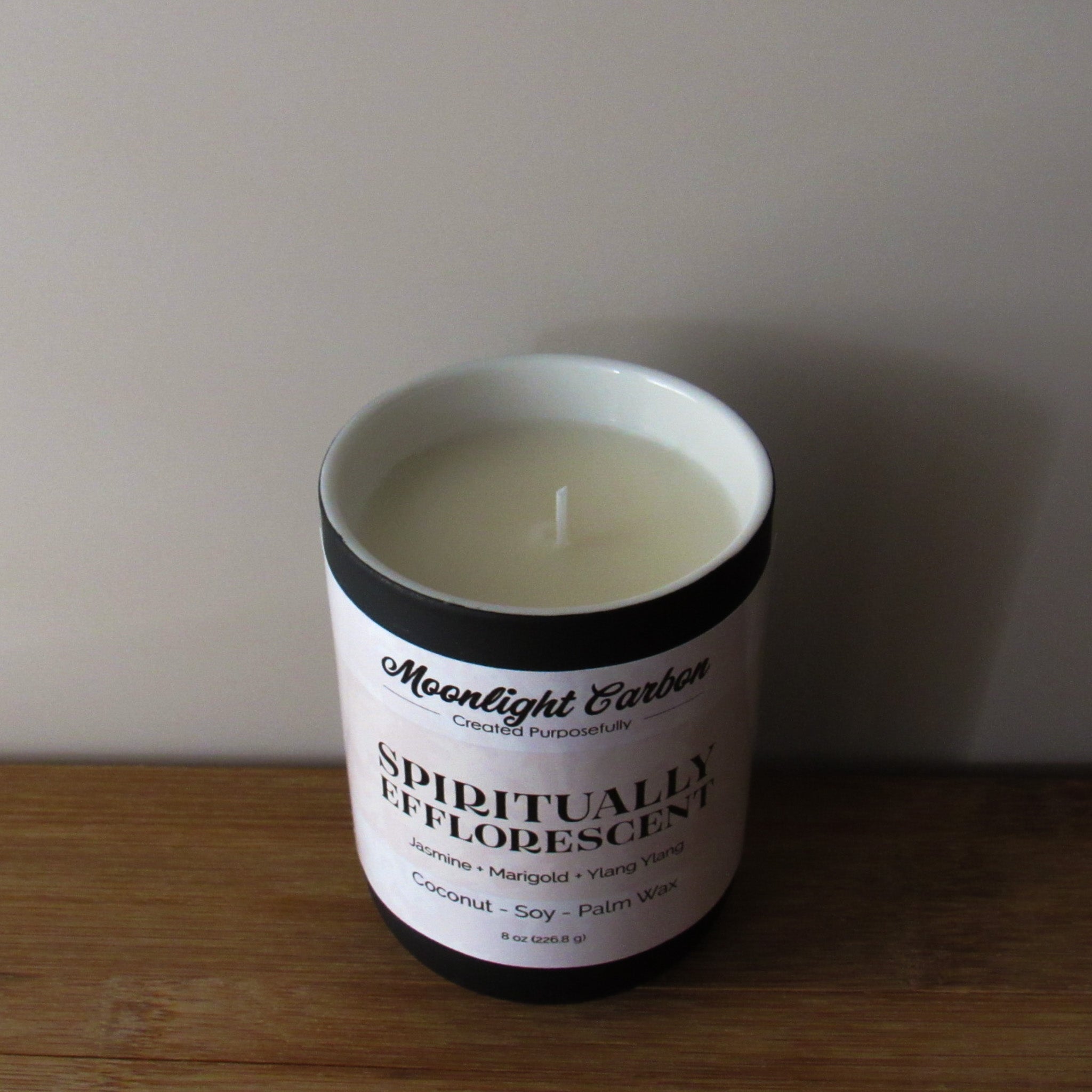 Zoomed in look at the coconut soy wax candle in a black ceramic container with beige label on a wooden surface. In the center of the candle is a cotton wick.