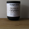 Candle jar labeled 'Tranquil Oasis' by Moonlight Carbon on a wooden surface with a neutral background. Fragrance notes include palo santo, lemon lavender. 