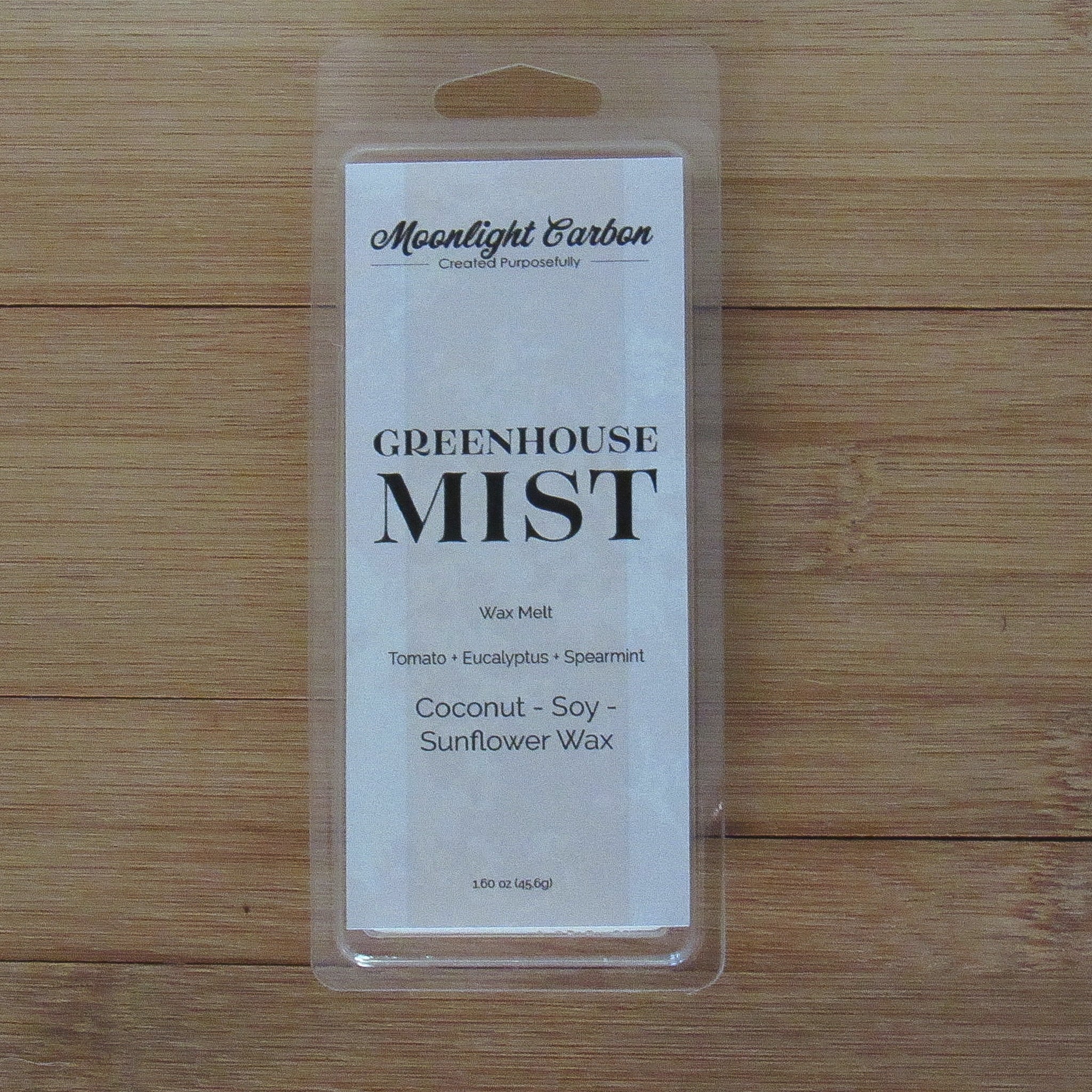 Wax melt packaging labeled 'Greenhouse Mist' on a wooden surface. Fragrance notes include tomato, eucalyptus, and spearmint.