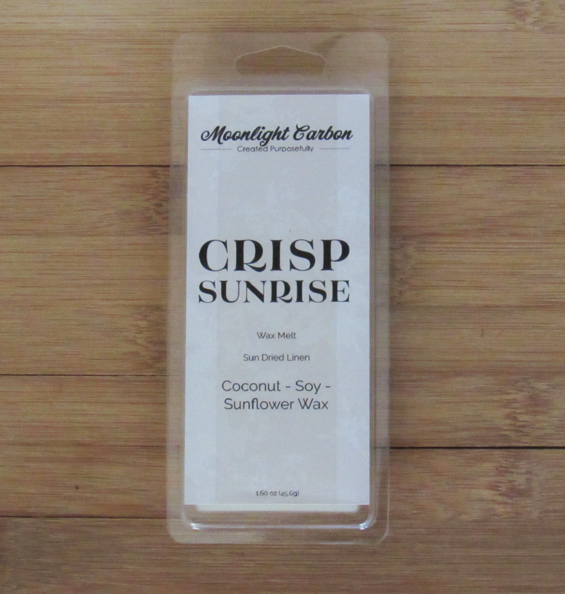 Packaged product labeled 'Crisp Sunrise' on a wooden surface. Fragrance notes include fresh laundry.