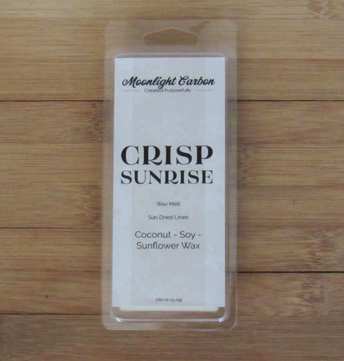 Packaged product labeled 'Crisp Sunrise' on a wooden surface. Fragrance notes include fresh laundry.