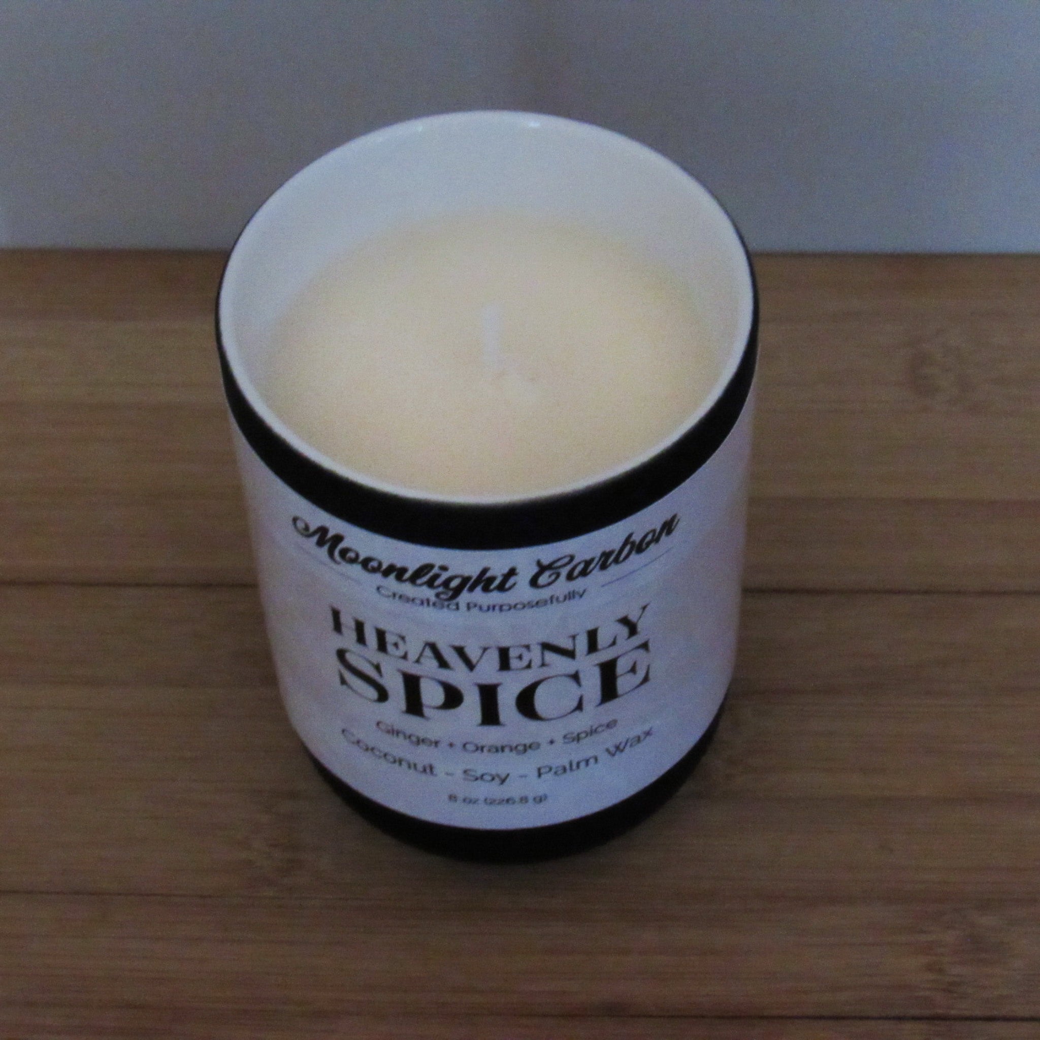 Candle in a white container with a label on a wooden surface. Zoomed in look into top of candle showing coconut, soy, palm was blend and cotton wick.