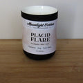 A candle labeled ‘Placid Flare’ in a black ceramic jar on a wooden surface.