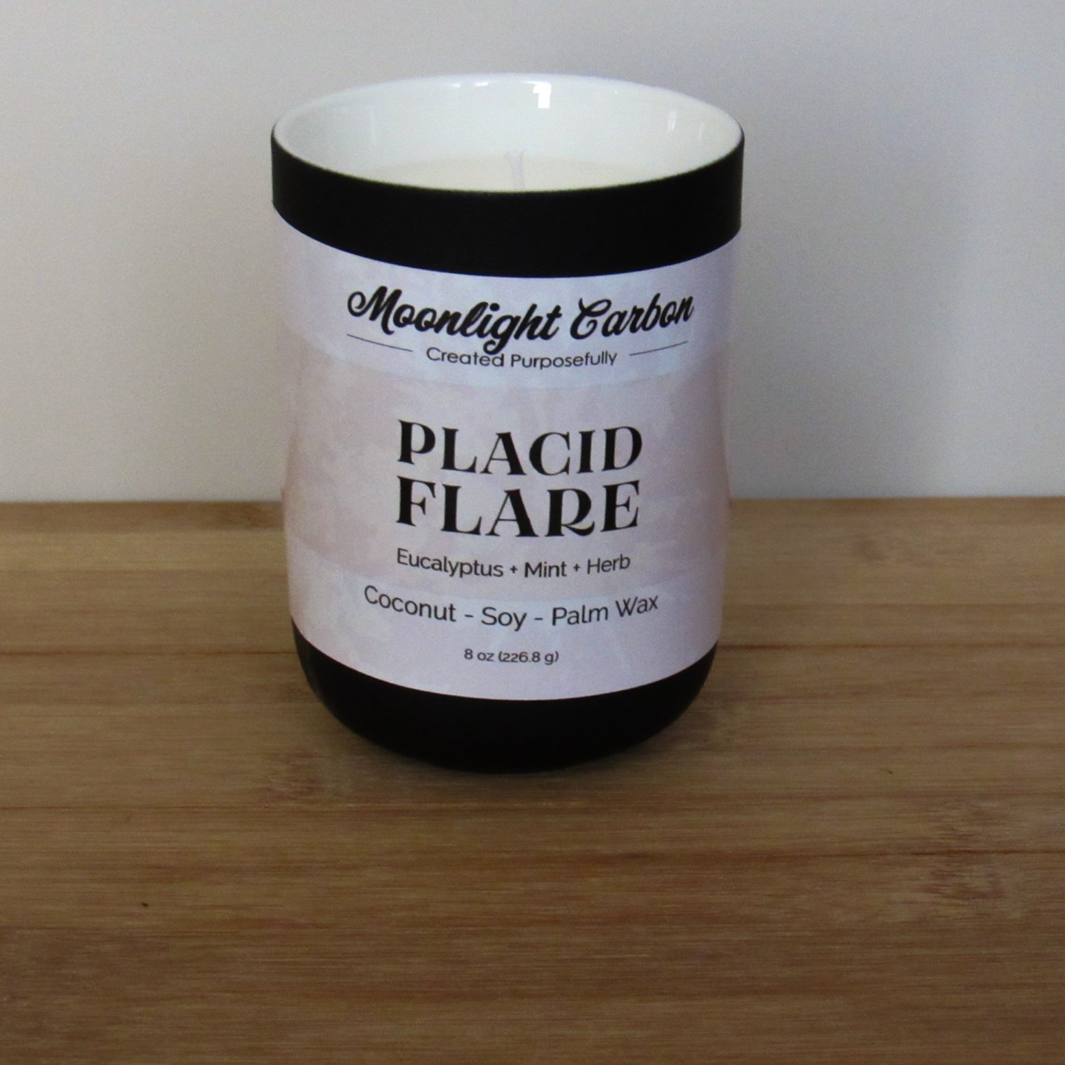 A candle labeled ‘Placid Flare’ in a black ceramic jar on a wooden surface.