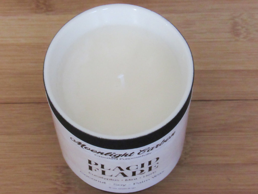 A candle on a wooden surface zoomed into the coconu, soy, palm wax top. In the center is a cotton wick.