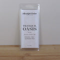 Packaged product labeled 'Tranquil Oasis' on a wooden surface with a neutral background. Fragrance notes include palo santo, lavender, and sage.