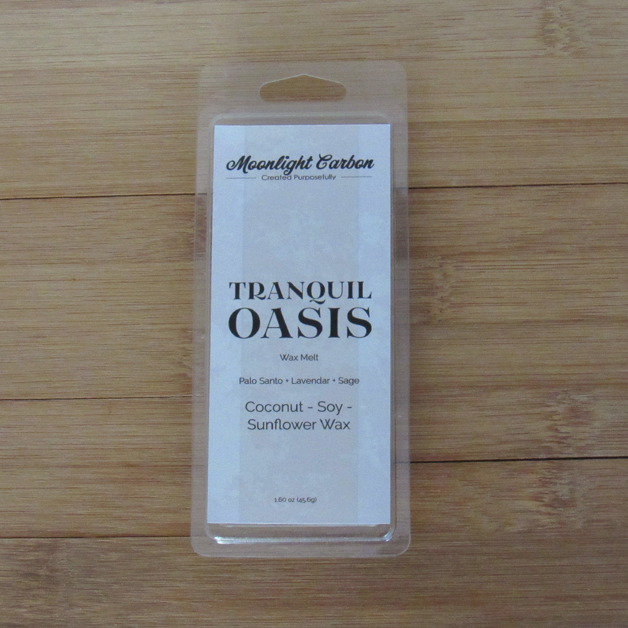 Packaged candle labeled 'Tranquil Oasis' on a wooden surface. fragrance notes include palo santo, lavender, and sage.