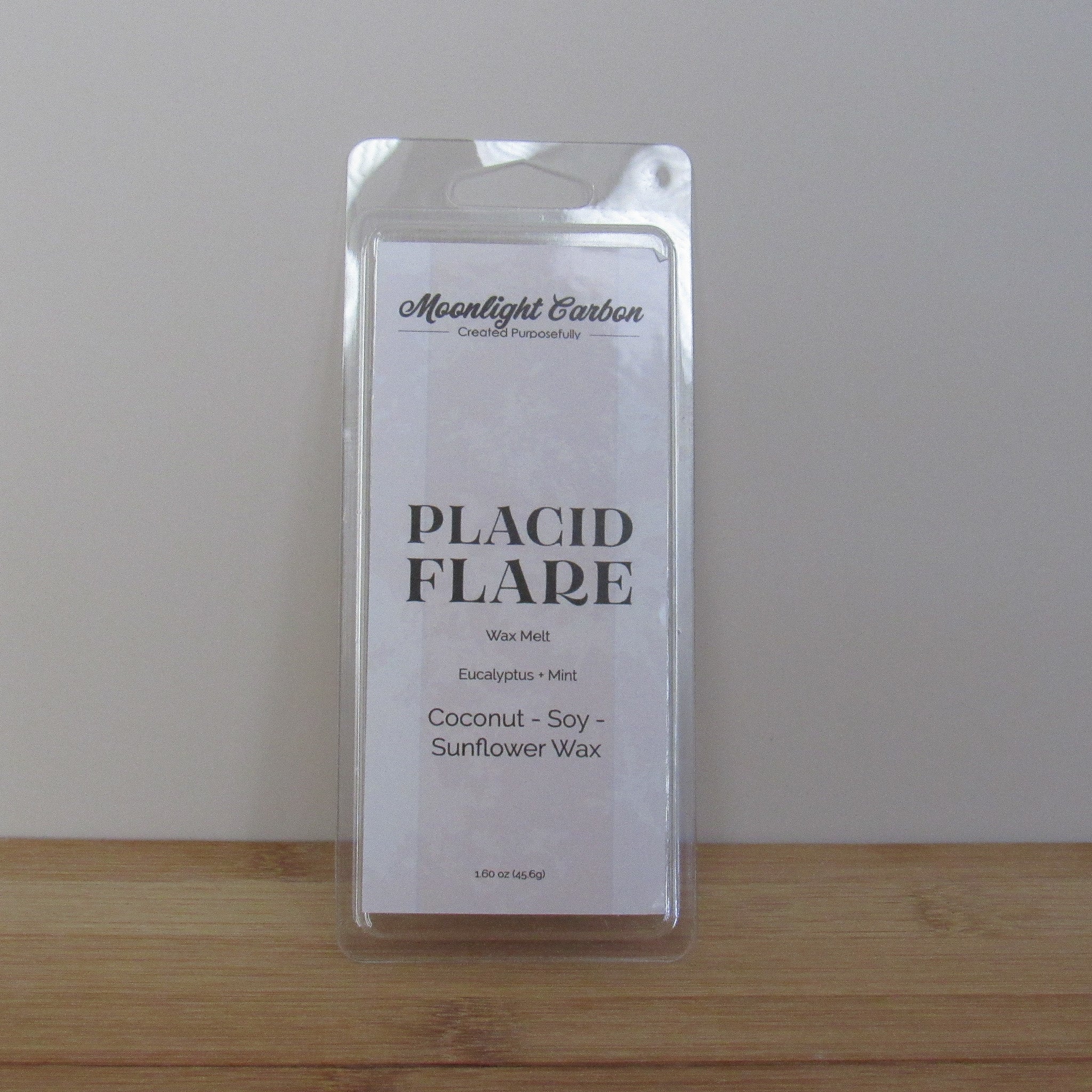 Packaged wax melt labeled 'Placid Flare' on a wooden surface with a neutral background. Fragrance notes include eucalyptus and mint.