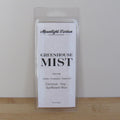 Packaged wax melt labeled 'Greenhouse Mist' by Moonlight Carbon on a wooden surface with a white background. Fragrance notes include tomato, eucalyptus, and spearmint.