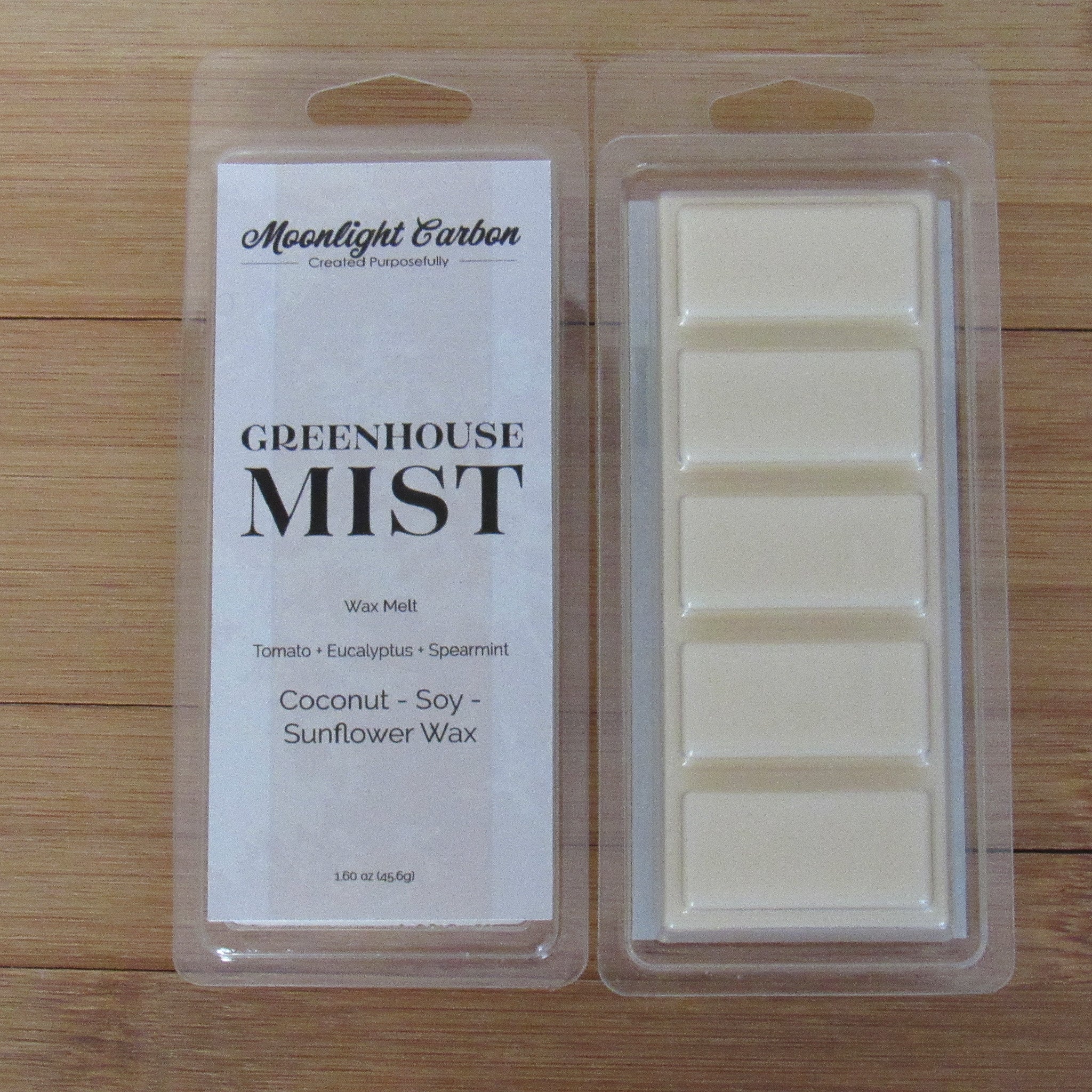 Wax melt packaging with 'Greenhouse Mist' label on a wooden surface. Show back of packaging with wax melts divided into 5 parts.