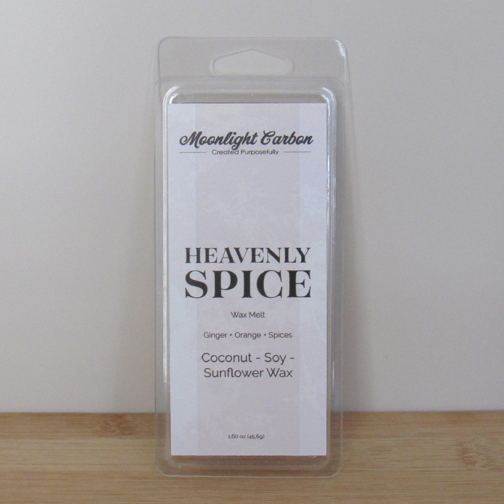 Packaged wax melt labeled 'Heavenly Spice' on a wooden surface with a neutral background. Fragrance notes include ginger, orange, and spices.