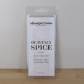 Packaged wax melt labeled 'Heavenly Spice' on a wooden surface with a neutral background. Fragrance notes include ginger, orange, and spices.