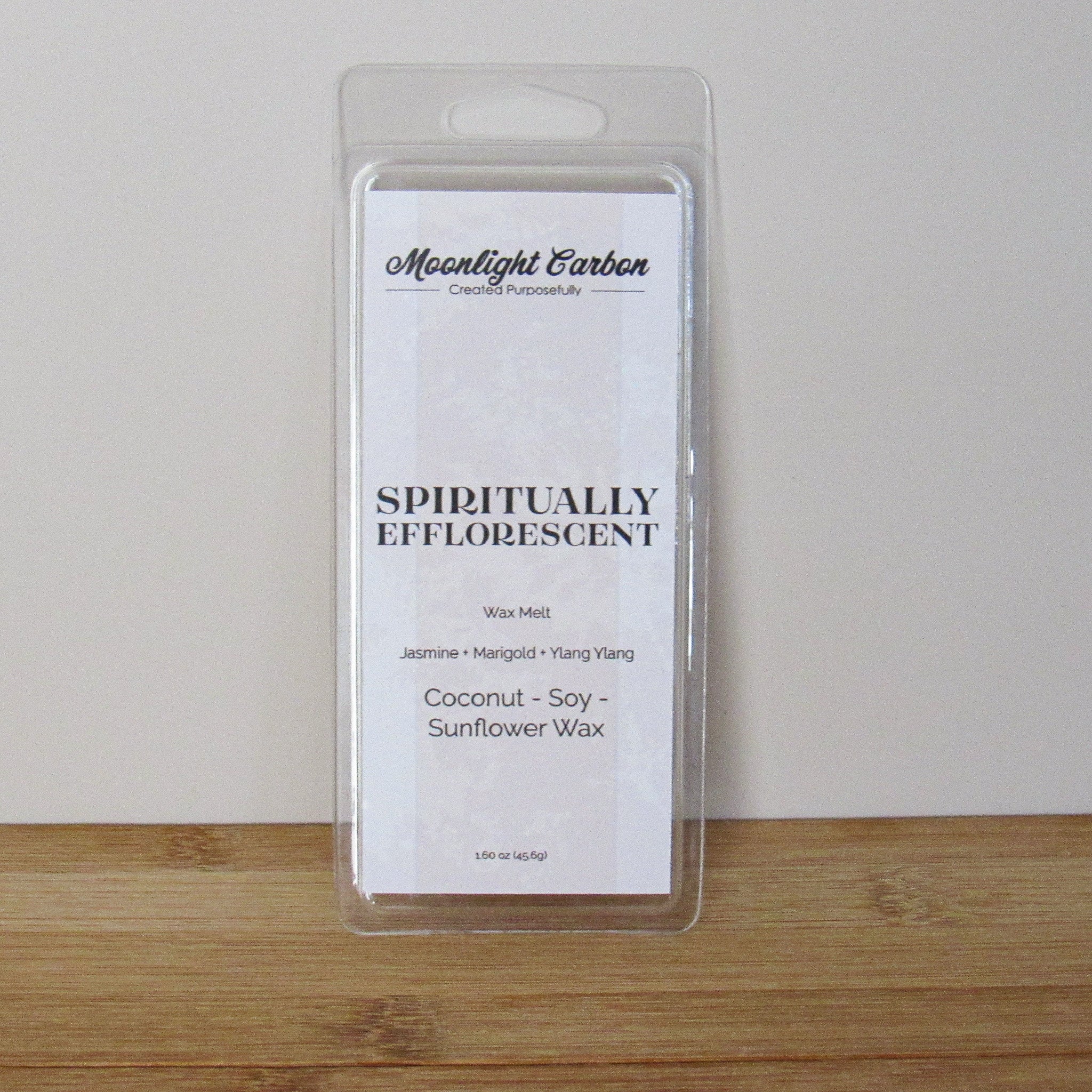 Packaged wax melt with branding and product details on a wooden surface. Fragrance notes include jasmine, marigold, and ylang ylang. 