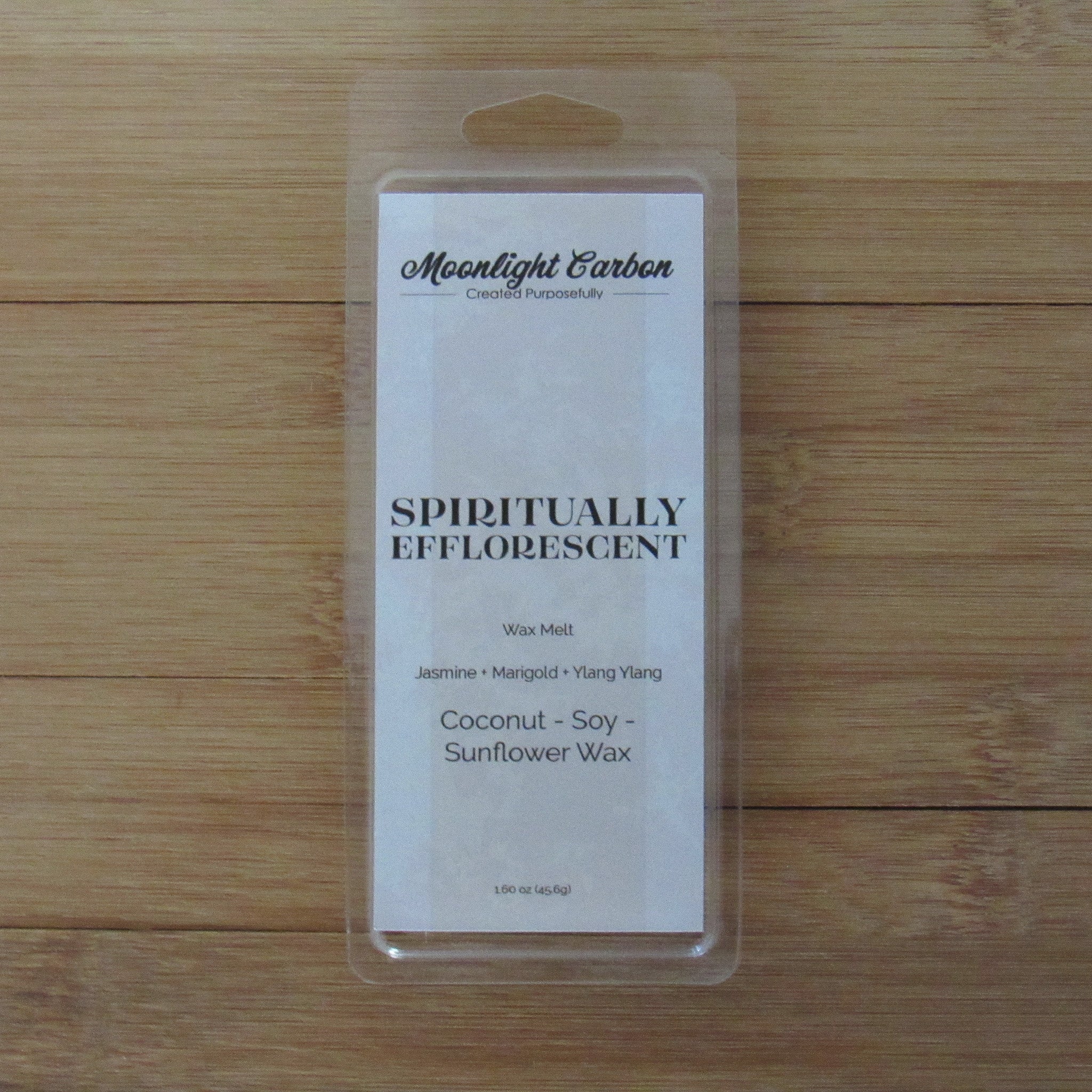Wax melt package labeled 'Spiritually Efflorescent' on a wooden surface. Fragrance notes include jasmine, marigold, and lang ylang.