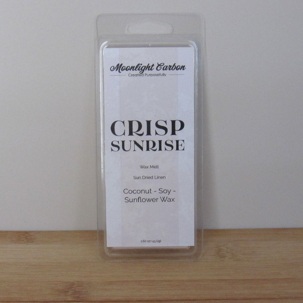 Packaged wax melt labeled 'Crisp Sunrise' by Moonlight Carbon on a wooden surface with a white background. Fragrance notes include fresh laundry.