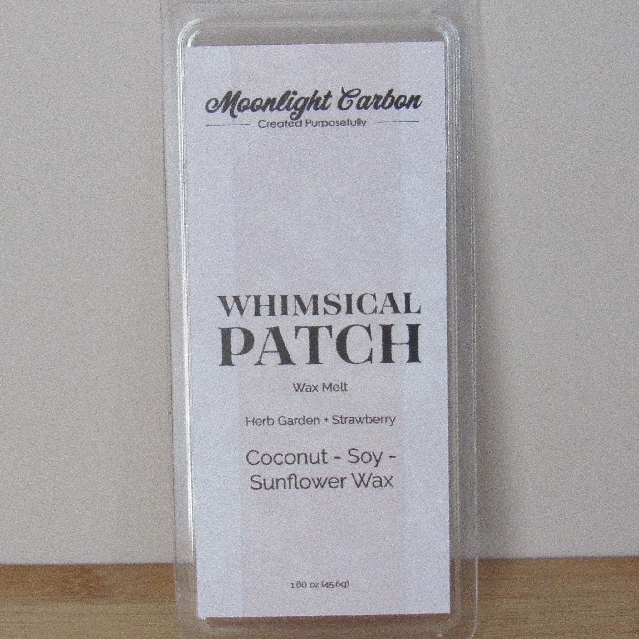 Wax melt package labeled 'Whimsical Patch' with branding on a plain background. Fragrance notes include herbal garden and strawberries. 