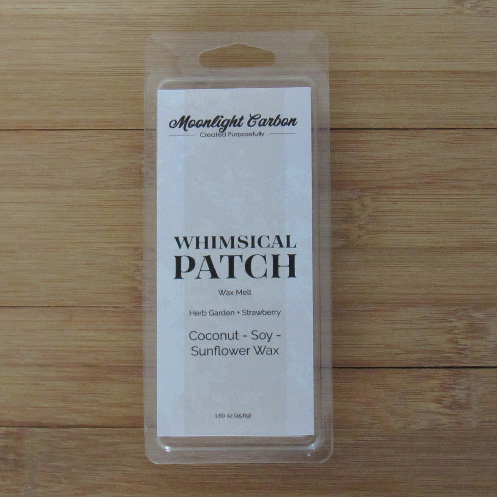 Packaged product labeled 'Whimsical Patch' on a wooden surface. Fragrance notes include herbal garden and strawberries. 
