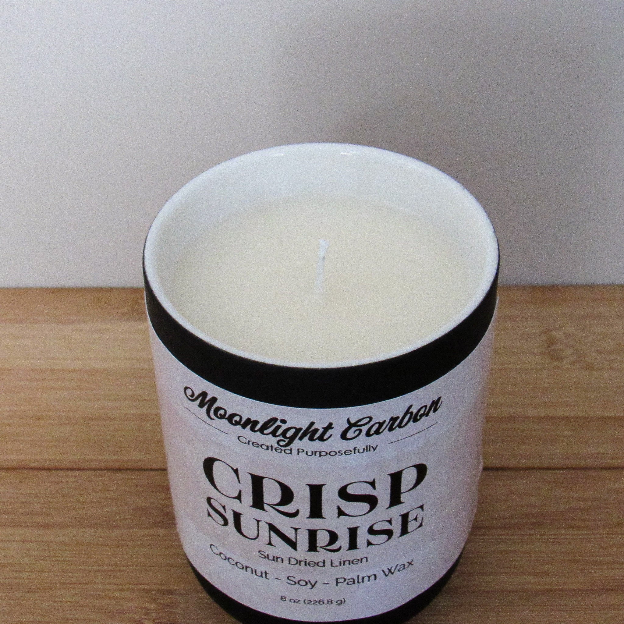 Candle in a white container with 'Moonlight Carbon' branding on a wooden surface. Zoomed in view into  top of candle showing coconut, soy palm wax blend and cotton wick