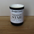 Candle labeled 'Crimson Star' on a wooden surface. Fragrance notes include Indian chai and oat milk. 