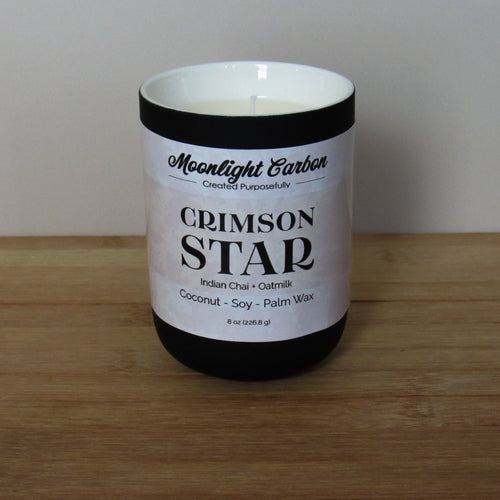 Candle labeled 'Crimson Star' on a wooden surface. Fragrance notes include Indian chai and oat milk. 