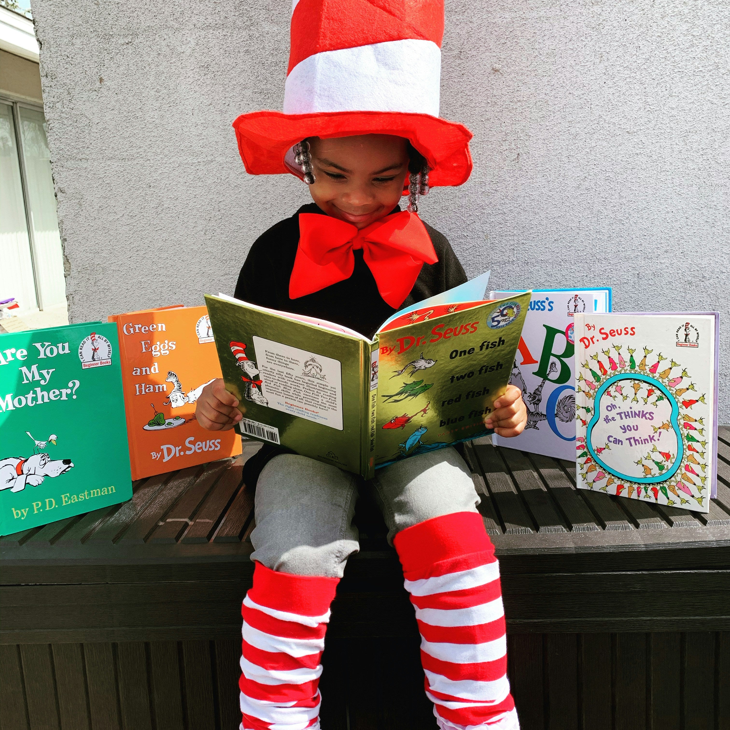 Child in a Dr. Seuss costume reading a book with Dr. Seuss books displayed around.